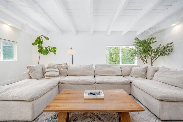 Una sala de estar moderna con un sofá seccional, una mesa de centro de madera y ventanas amplias.
