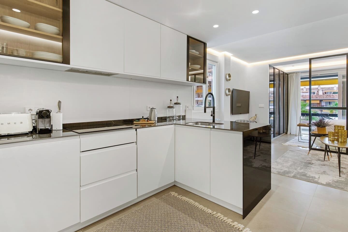 A modern kitchen with white cabinetry, a built-in oven, and a dining area with a table and chairs.