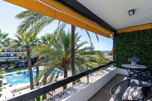 A balcony with a view of a pool, palm trees, and a green wall.