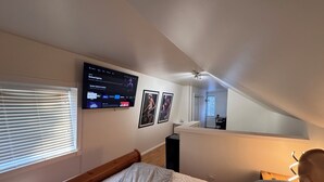 Une chambre à coucher avec un lit, un téléviseur fixé au mur et un ventilateur de plafond.