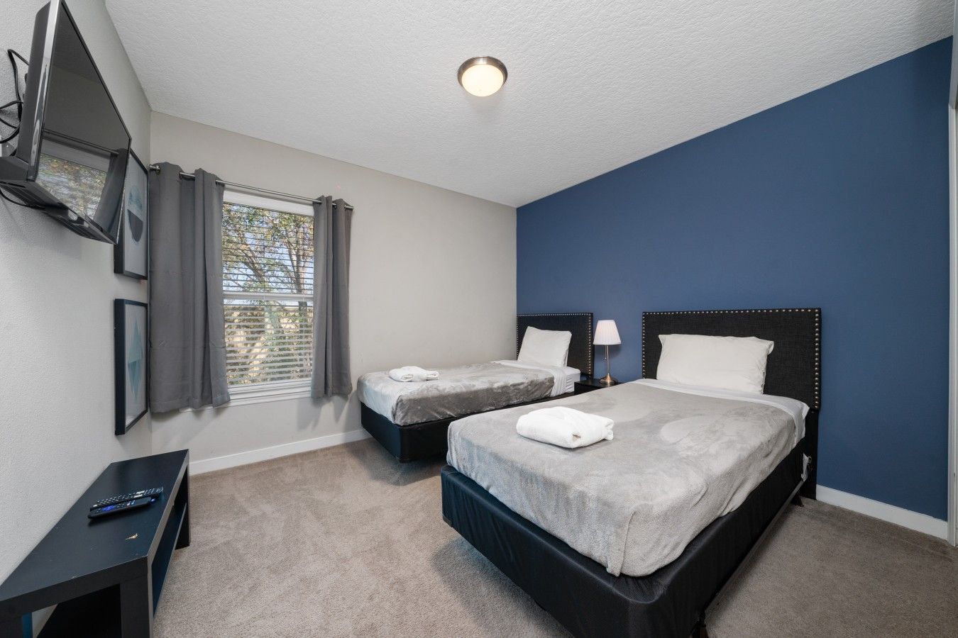 A bedroom with two beds, a desk, a TV, and a window with curtains.
