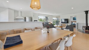 Een moderne keuken met een groot eiland, een eethoek met een houten tafel en stoelen, en een zithoek met een bank en televisie.
