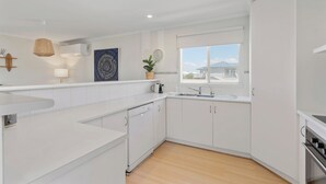 Een moderne keuken met witte kastjes, een inbouwoven en een raam met uitzicht op een huis en bergen.