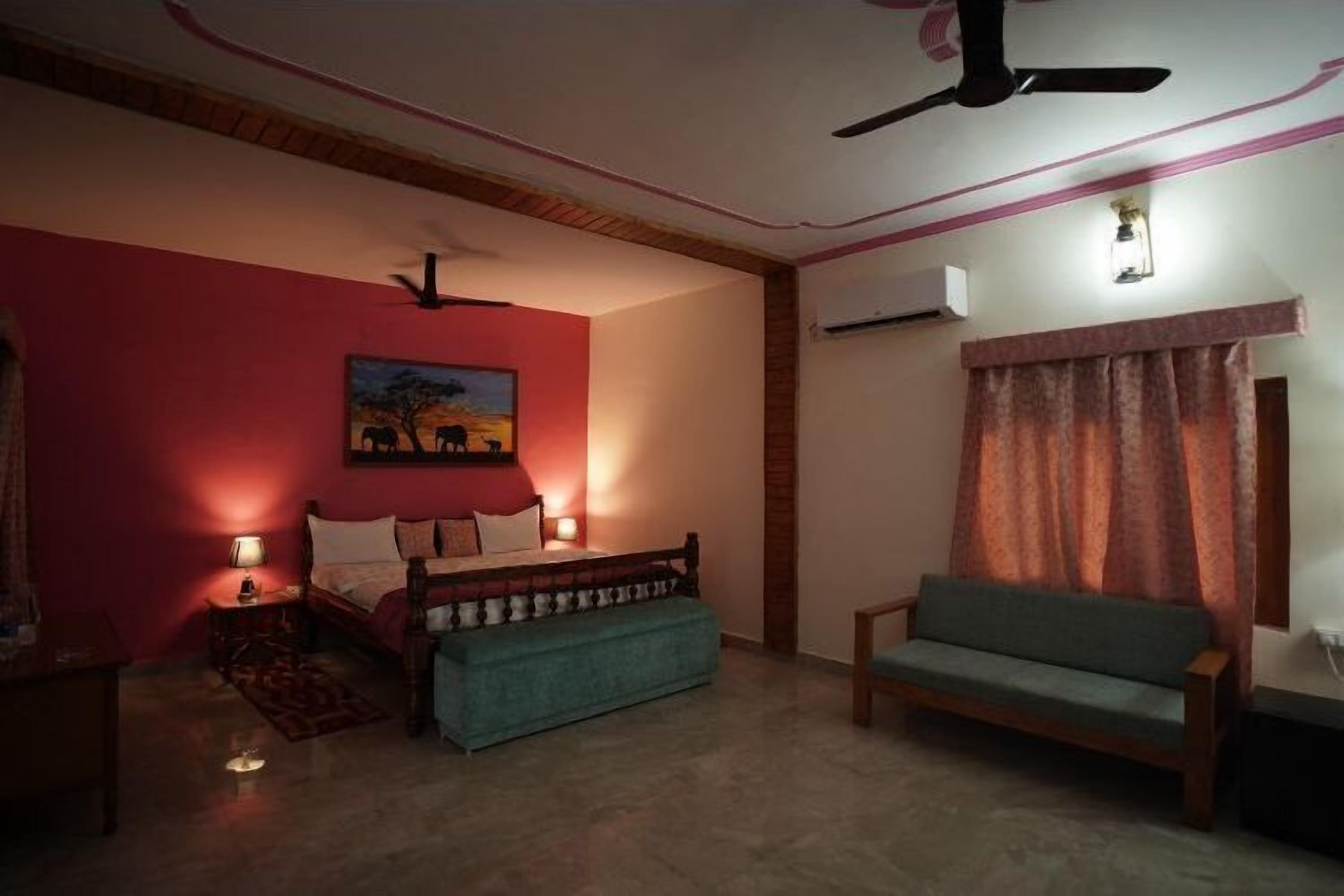 A bedroom with a bed, a sofa, a ceiling fan, a painting, and a window with curtains.