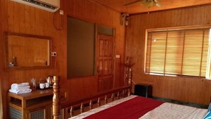 Una stanza con rivestimenti in legno, un letto, una panca di legno, una finestra con persiane e un condizionatore d'aria a muro.