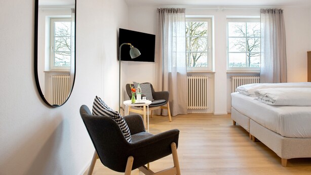 A hotel room with a bed, a chair, a TV, and two windows with curtains. - Room 'Konstanz' with Shared Terrace, Shared Garden and Wi-Fi (Salem)