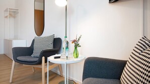 A modern room with a round table, two chairs, a mirror, a floor lamp, a small vase with flowers, and a television mounted on the wall. - Room 'Konstanz' with Shared Terrace, Shared Garden and Wi-Fi (Salem)