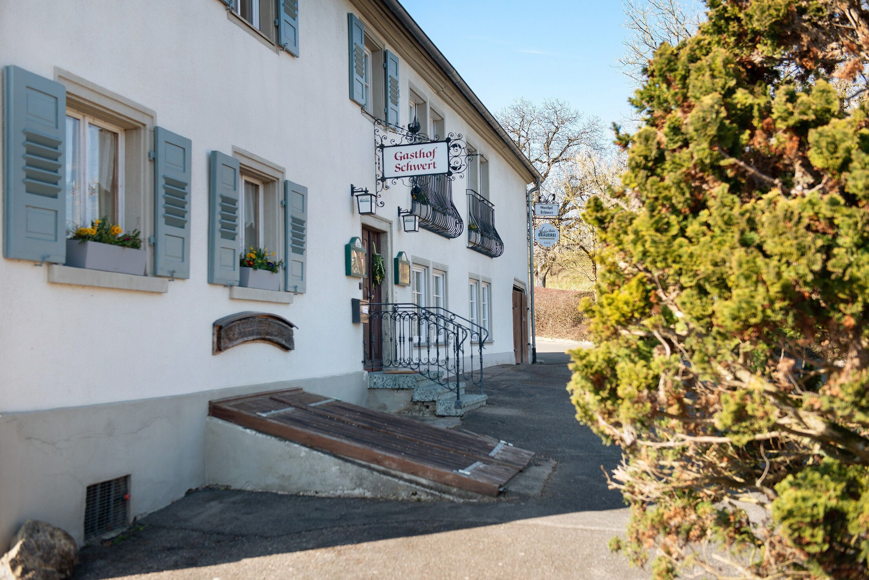 Ein Gebäude mit einem Schild, auf dem 'Gasthof Schwert' steht, einer Treppe, die zum Eingang führt, und einer kleinen Gartenanlage mit Pflanzen.