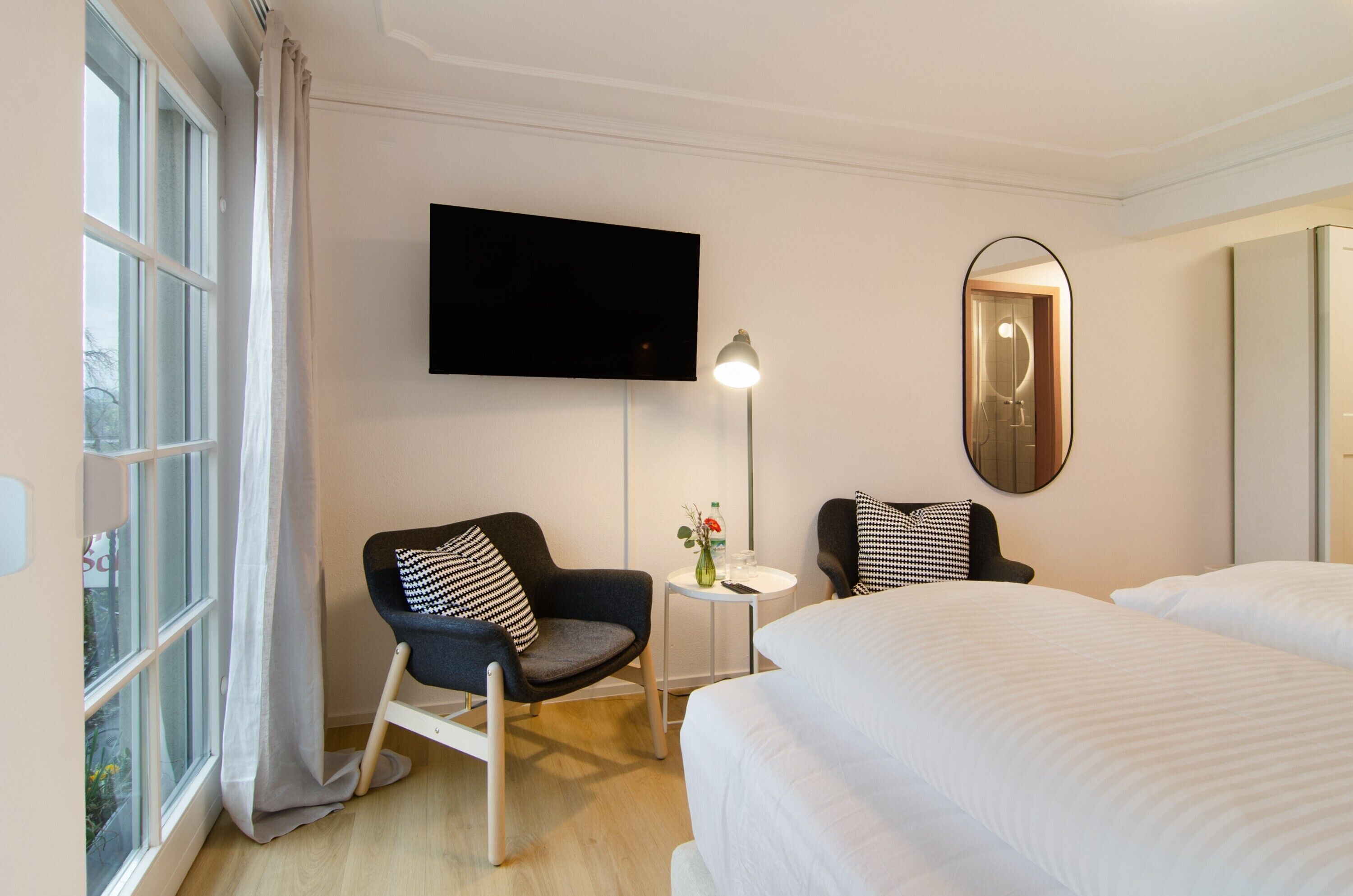 Quarto de hotel com duas camas, uma televisão, um espelho, um abajur e uma janela com cortinas.