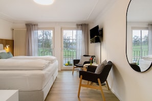 A hotel room with two beds, a desk, a chair, a TV, and large windows.