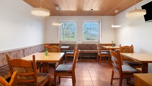 A dining area with wooden tables and benches, large windows, and pendant lighting. - Room 'Meersburg' with shared terrace and Wi-Fi (Salem)