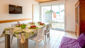 A dining area with a table set for two, a television mounted on the wall, and a sliding glass door leading to an outdoor area. - Ker Zelia by Interhome (La Bernerie-en Retz)