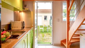 A modern kitchen with green cabinets, a wooden ceiling, and a view of a garden through an open door. - Ker Zelia by Interhome (La Bernerie-en Retz)