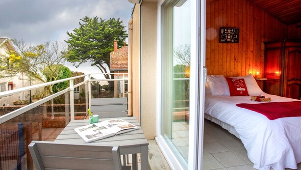 A bedroom with a bed, a window, and a balcony with a table and chair. - Ker Zelia by Interhome (La Bernerie-en Retz)