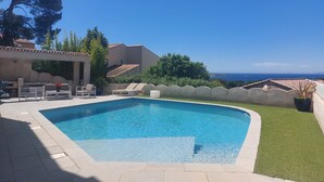 Ein Pool mit Meerblick, umgeben von einer Terrassenanlage mit Stühlen und einem Tisch.