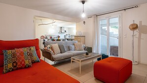 Ein modernes Wohnzimmer mit Sofa, Hocker und Couchtisch. Im Hintergrund ist eine Küche erkennbar.