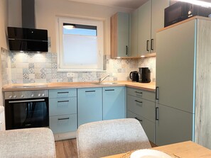 Eine kompakte Küche mit Backofen von Bosch, einer Mikrowelle und einer Kaffeemaschine. Ein Fenster mit Jalousien und die Schränke sind hellblau.