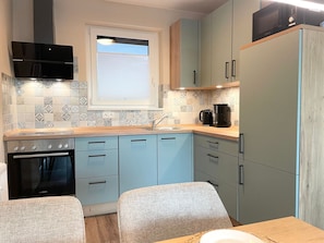 A compact kitchen with a Bosch oven, a microwave, and a coffee maker. There is a window with blinds, and the cabinets are light blue.