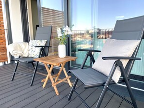 Ein Balkon mit zwei Stühlen, einem kleinen Tisch und einer Vase mit Blumen.