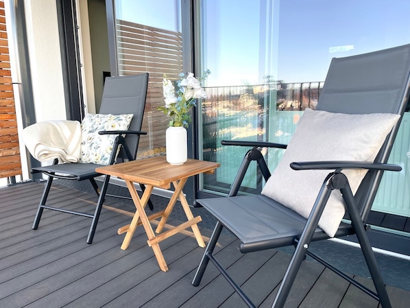 A balcony with two chairs, a small table, and a vase with flowers.