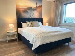 Une chambre à coucher avec un grand lit, deux tables de chevet, une commode, une fenêtre avec des rideaux et une fresque murale.