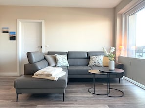 A modern living room with a grey sectional sofa, a small round table, and a vase with flowers.