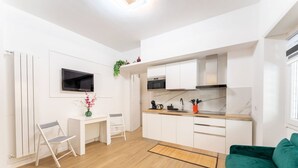 Een compacte keuken met witte kastjes, een magnetron en een kleine eethoek met een stoel en tafel.