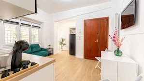 Een moderne keuken met een koffieapparaat, een eethoek met een witte tafel en stoelen, en een woonkamer met een groene bank.