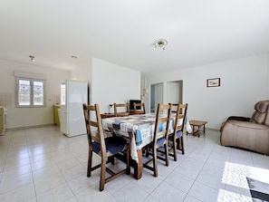 Un vaste espace de vie comprenant une table à manger, des chaises en bois, un canapé et un coin cuisine équipé d’un réfrigérateur.