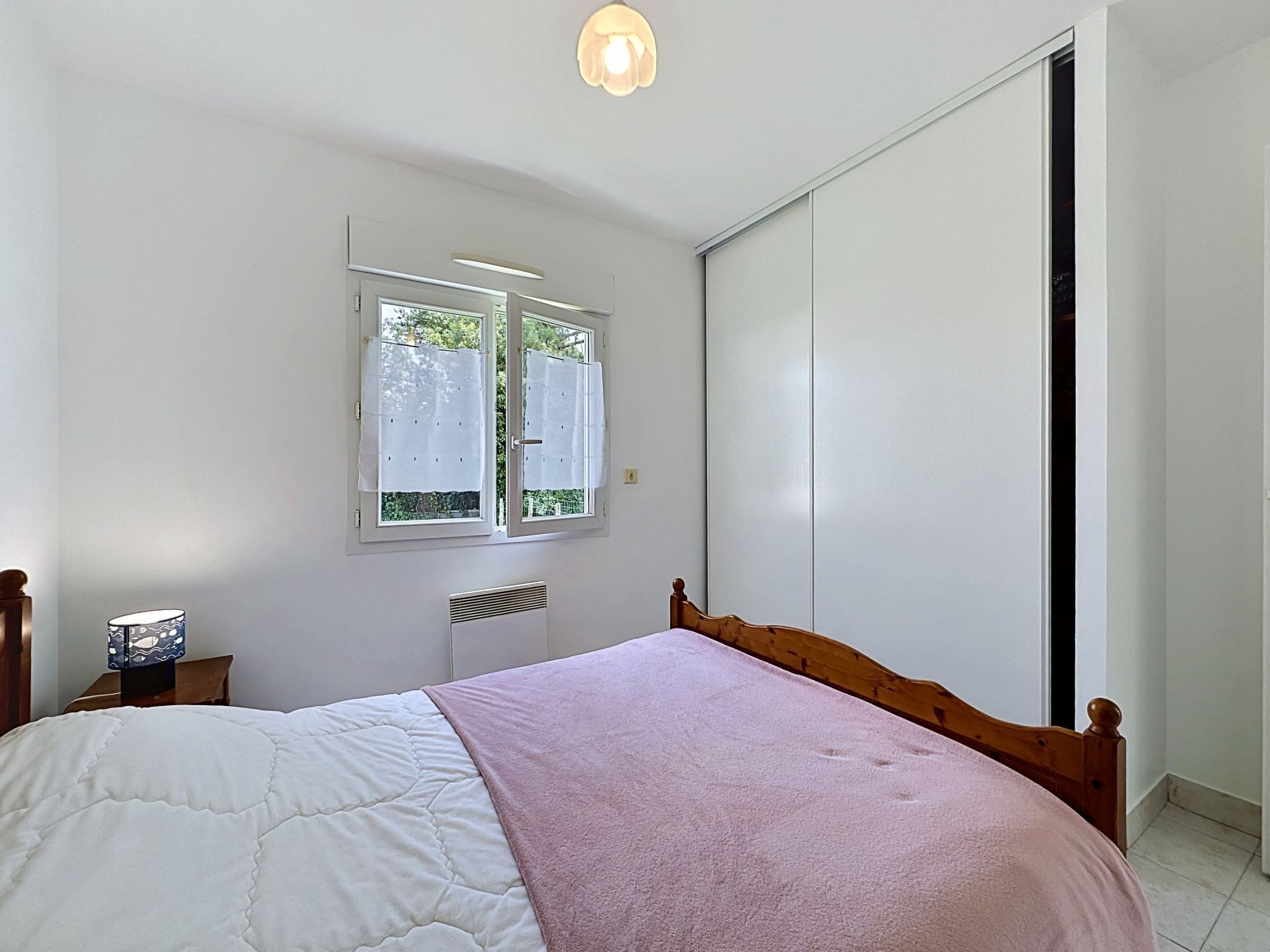 Een slaapkamer met een bed, een raam met gordijnen, een radiator en een kledingkast.