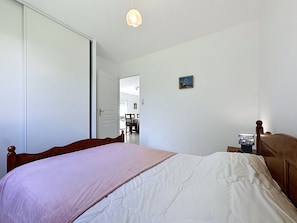 Une chambre à coucher avec un lit, une table de chevet, une lampe, une porte et un petit tableau accroché au mur.