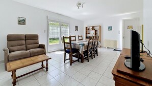 Un salon comprenant un canapé, une table à manger avec des chaises, un téléviseur posé sur un meuble et une bibliothèque.