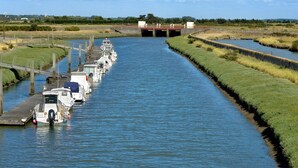 Un canal bordé de bateaux amarrés sur la rive gauche, un pont en arrière-plan et des berges verdoyantes de chaque côté.