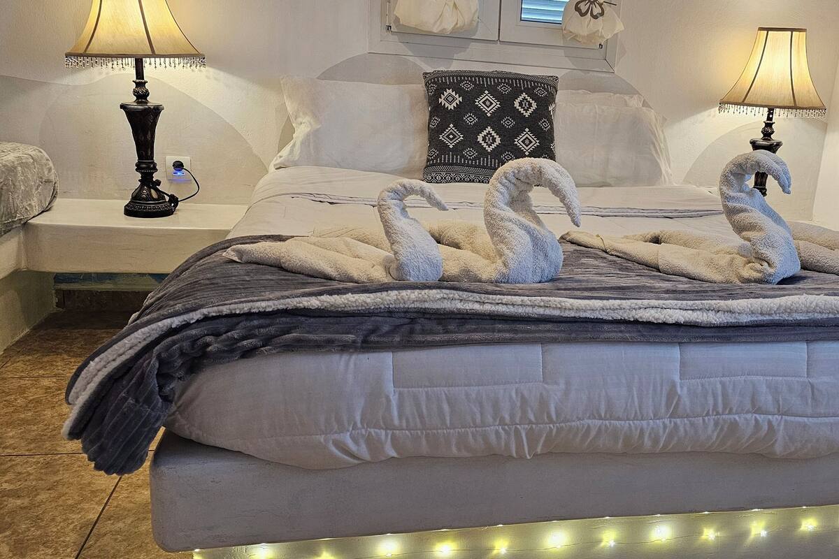 Una cama bien hecha con un edredón blanco y esponjoso, dos lámparas de noche y un arreglo decorativo de toallas sobre la cama.