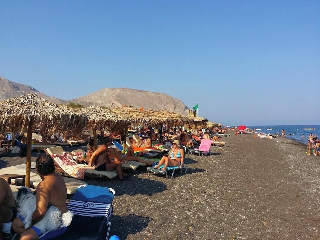 A beach with sun loungers and umbrellas, a clear sky, and a rocky landscape in the background.