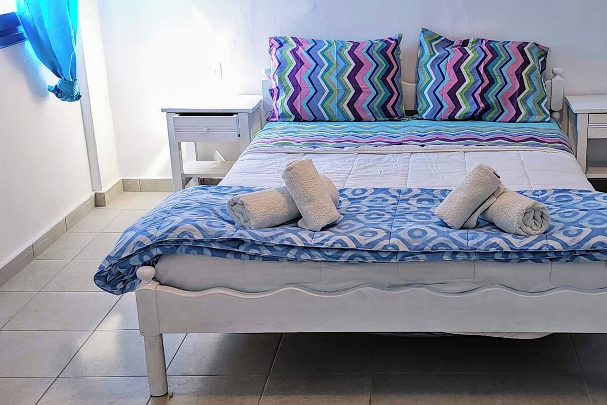 Una cama con una colcha estampada, dos almohadas y dos toallas.