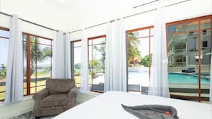 A hotel room with a large bed, a sofa, and a view of a swimming pool and palm trees.