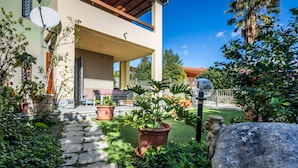 Uma casa moderna com varanda coberta, plantas em vasos e um caminho de pedra.