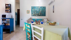 Uma sala de jantar com mesa posta para quatro, cadeiras, um quadro na parede e um aparelho de ar condicionado.
