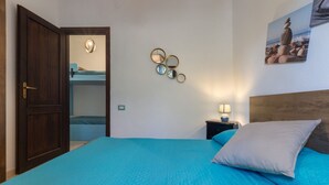 Quarto com uma cama, mesa de cabeceira, espelho fixado na parede e uma porta.