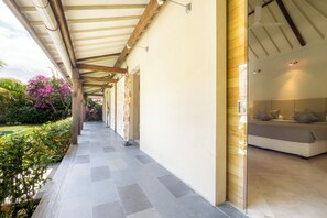 Ein überdachter Außenbereich mit Bett und Fenster, der zu einem Raum mit Gartenblick führt.