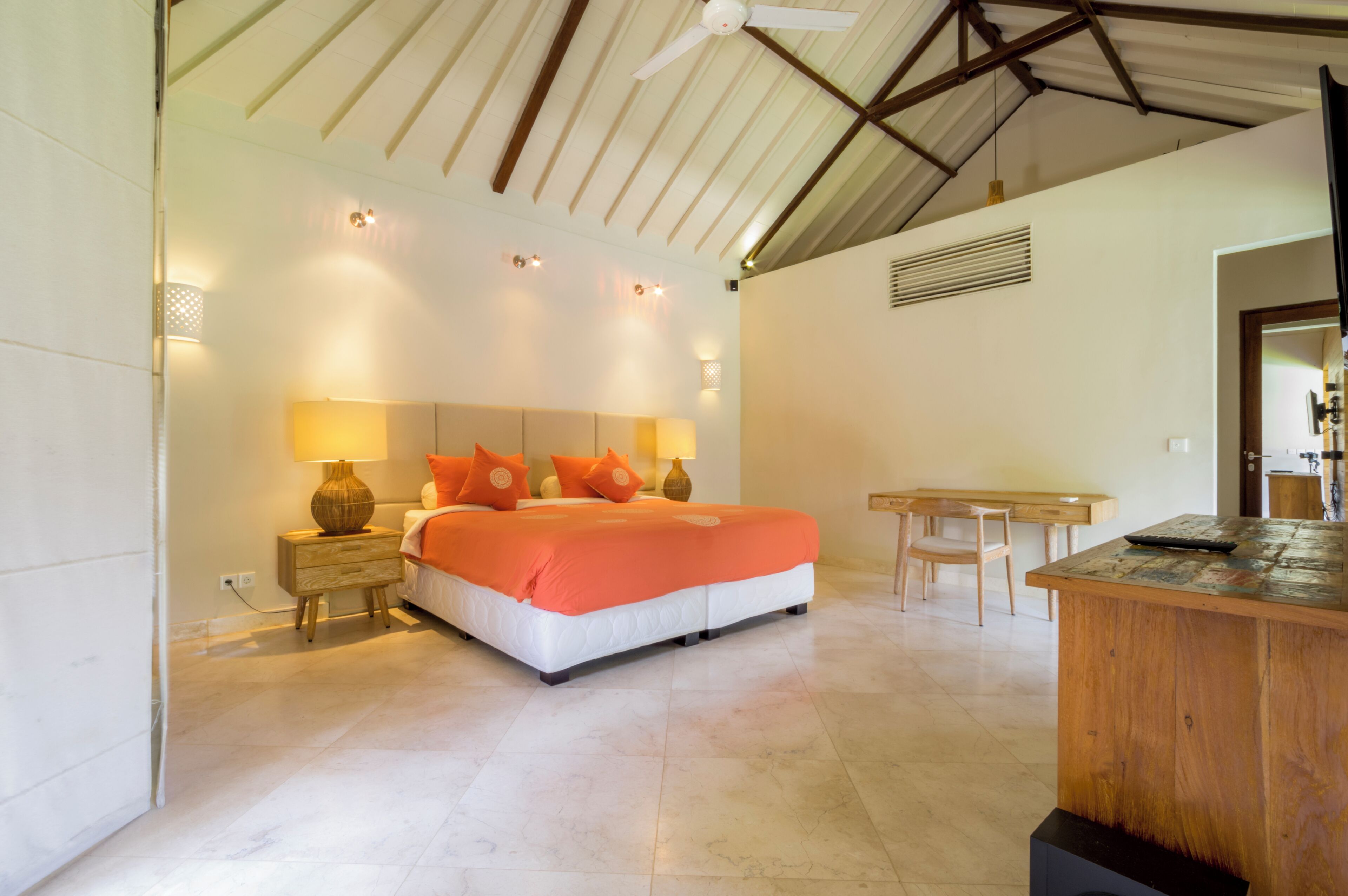 A bedroom with a bed, bedside table, lamp, and a wooden desk.