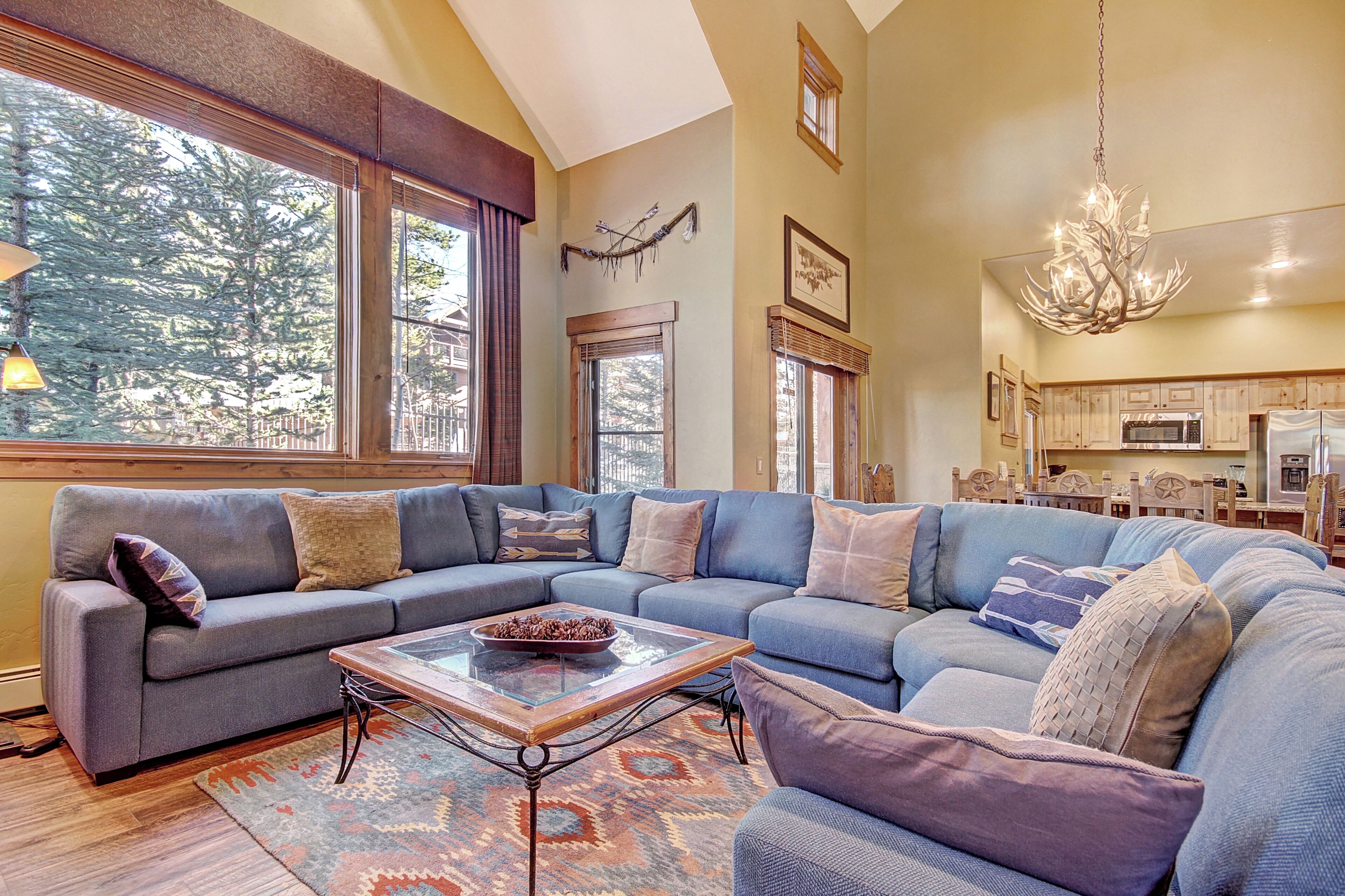 A spacious living room with a large sectional sofa, a glass coffee table, and a chandelier.