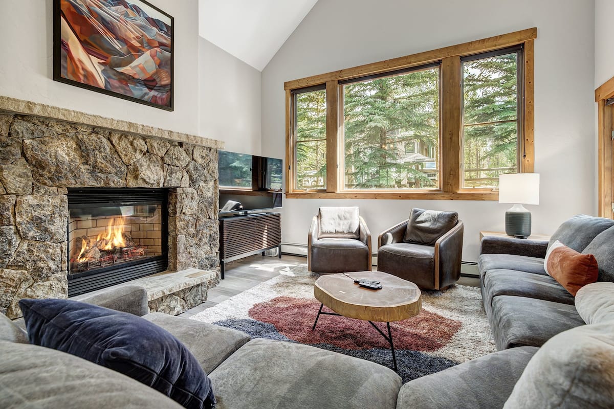 A living room with a stone fireplace, large windows, a sofa, and a coffee table.