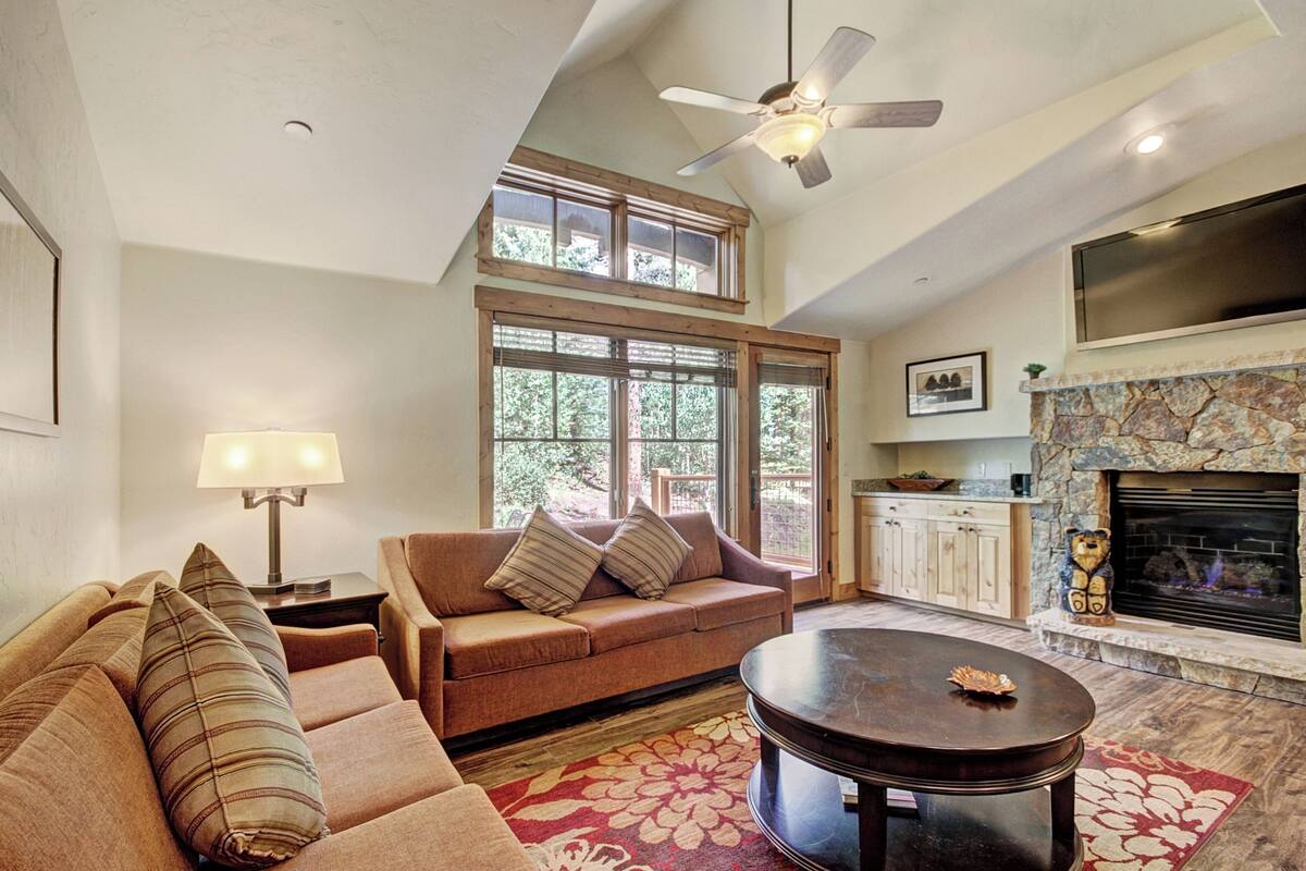 A living room with a high ceiling, a fireplace, a sofa, a coffee table, and a TV mounted on the wall.