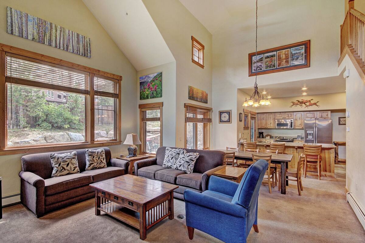 A spacious living area with a large window, a sofa, a coffee table, and a dining table with chairs.