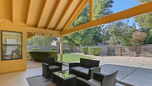 Un patio techado con muebles de mimbre y vistas al jardín trasero.