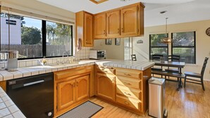 Una cocina con armarios de madera, lavavajillas, pileta y comedor con mesa y sillas.