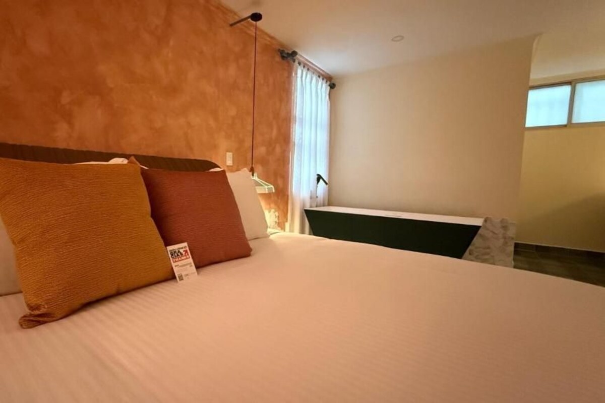 A hotel room with a bed, pillows, a nightstand, and a window with curtains.