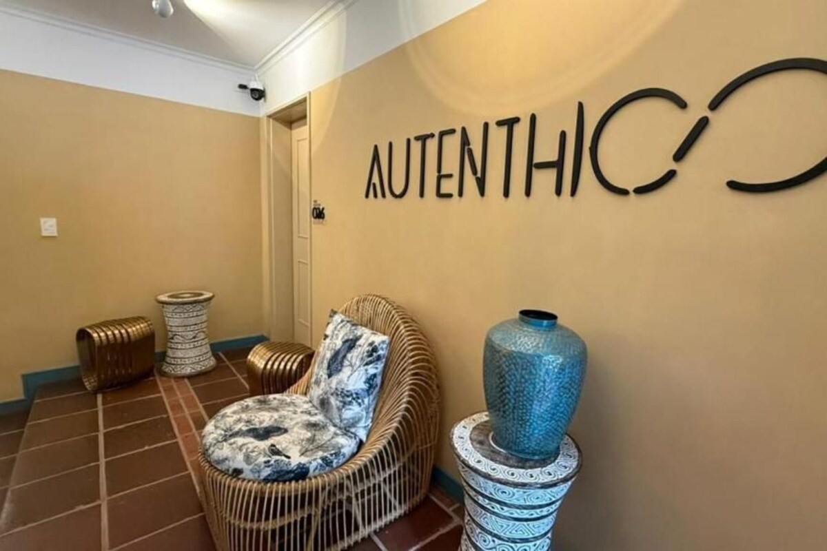 A reception area with a wicker chair, a decorative vase, and a wall-mounted sign reading "AUTHENTICO".